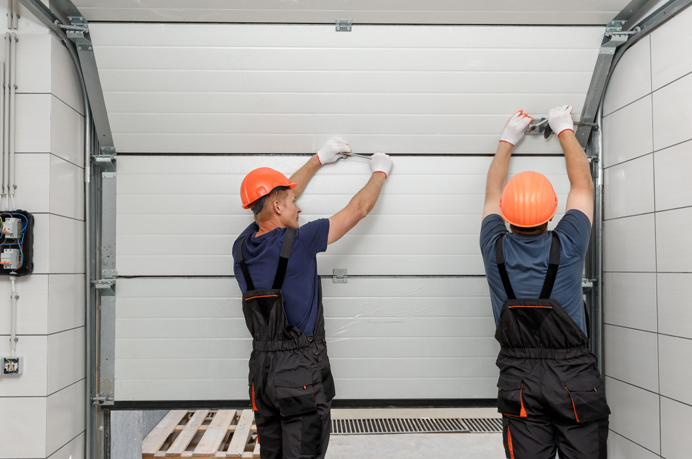 Two men with hard hats working on a garage door.