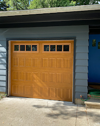 A light brown wooden garage door in a home with light blue siding.